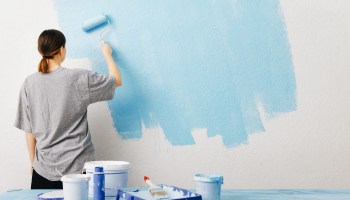 Una mujer pasando el rodillo por la pared de su casa.